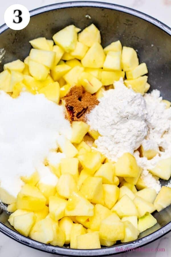 Dutch apple pie process photo 3 showing added sugar, apple pie spice, and flour to the bowl of chopped apples.