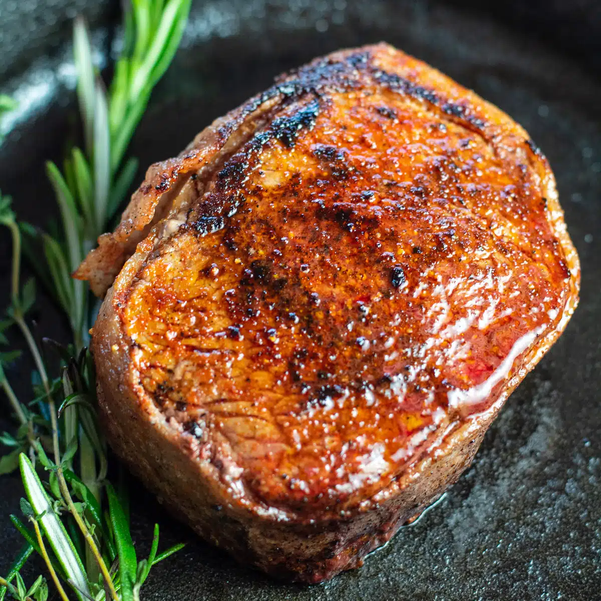 Square image of bacon wrapped filet mignon in a cast iron pan.