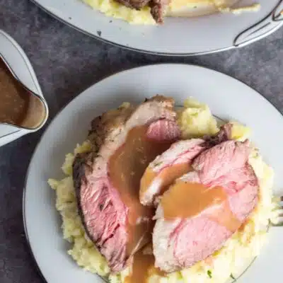 Tall image showing sliced instant pot chuck roast with mashed potatoes and gravy on a plate.