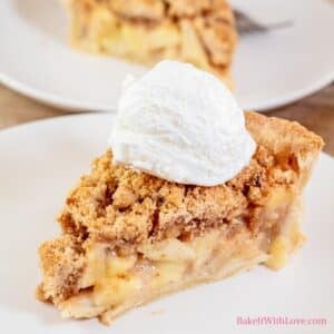 Dutch apple pie slice on white plate with whipped cream topping.