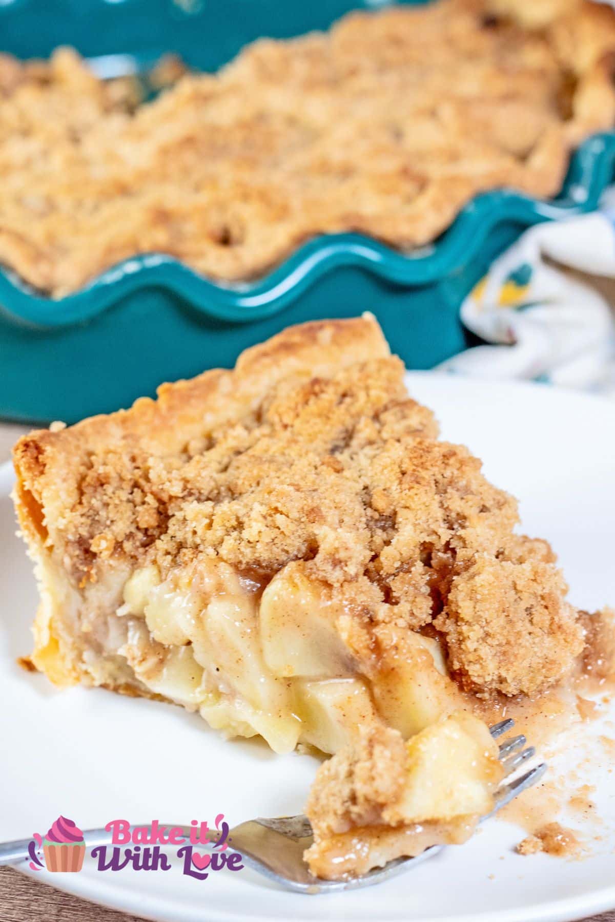 Tall image showing a slice of Dutch apple pie on a plate with a fork set in front of it and the remaining pie in the background. 