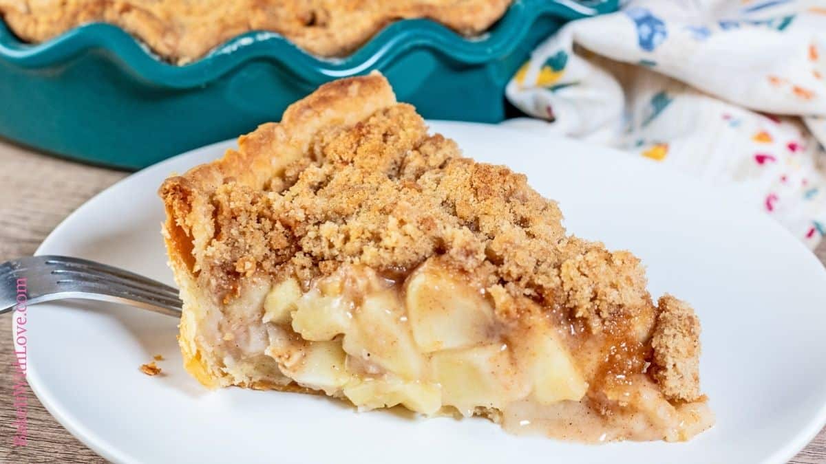 Wide image showing a slice of Dutch apple pie on a ceramic white plate with a fork set on the edge of the plate.