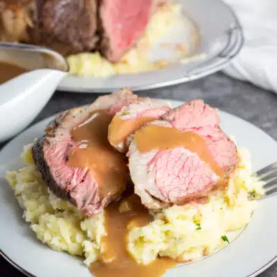 Square image showing sliced instant pot chuck roast with mashed potatoes and gravy on a plate.