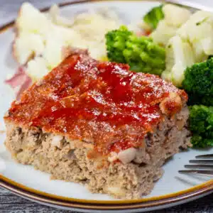 Square image of a slice of turkey meatloaf on a white plate.