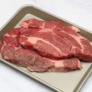 What is chuck steak illustrated with two large, raw chuck steaks stacked on metal sheetpan.