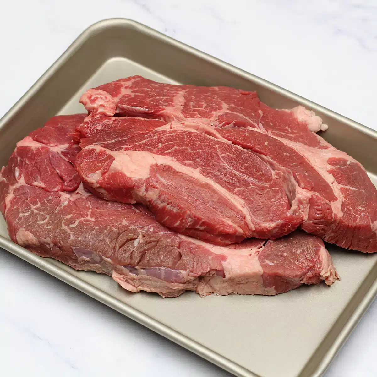 What is chuck steak illustrated with two  large, raw chuck steaks stacked on metal sheetpan.