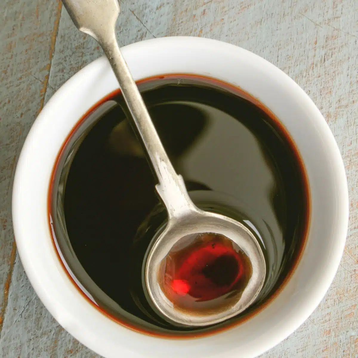 Square image showing balsamic reduction in a small white bowl.