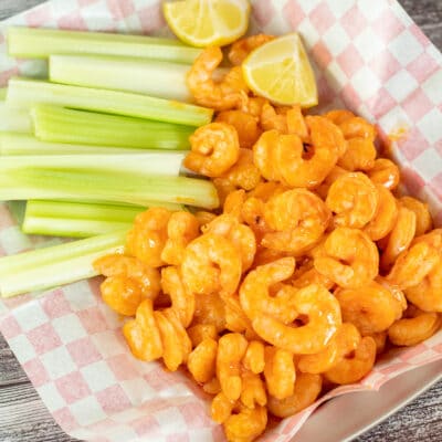 Square image showing buffalo shrimp in a basket with celery.