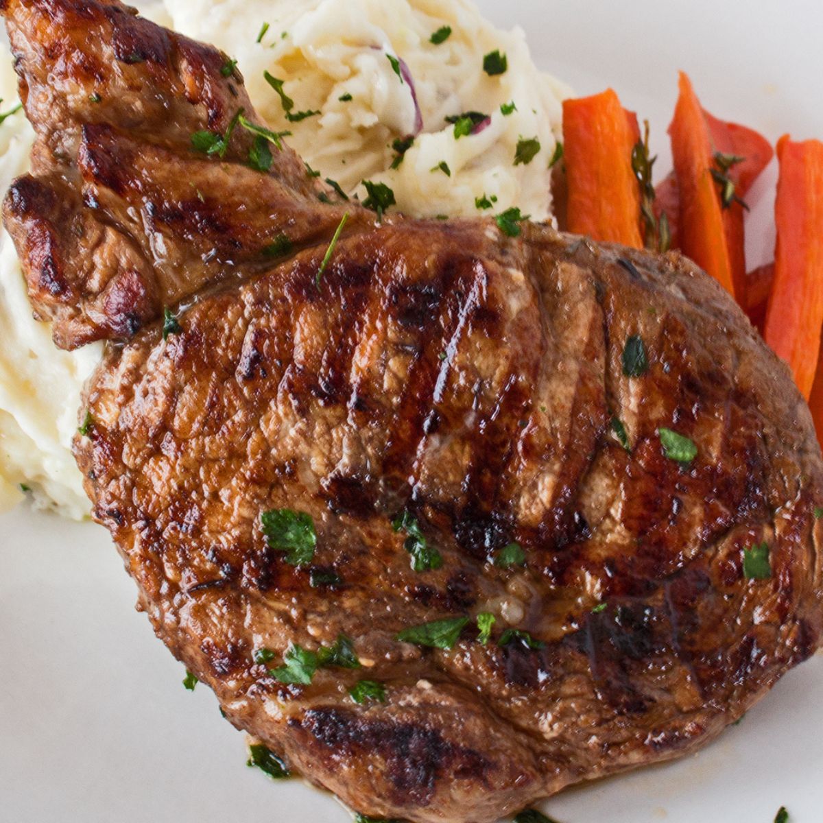 Square image of a pork chop on a plate.