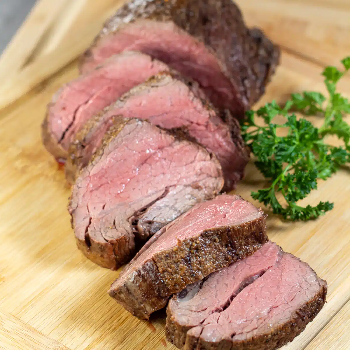 Square image of sliced chateaubriand on a cutting board.