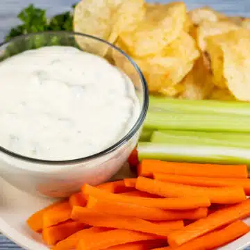 Wide image showing dill pickle dip with carrots, chips, and celery.