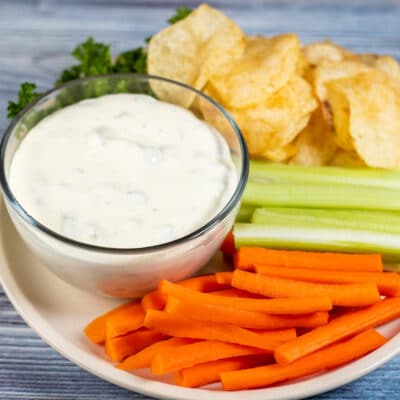 Square image showing dill pickle dip with carrots, chips, and celery.