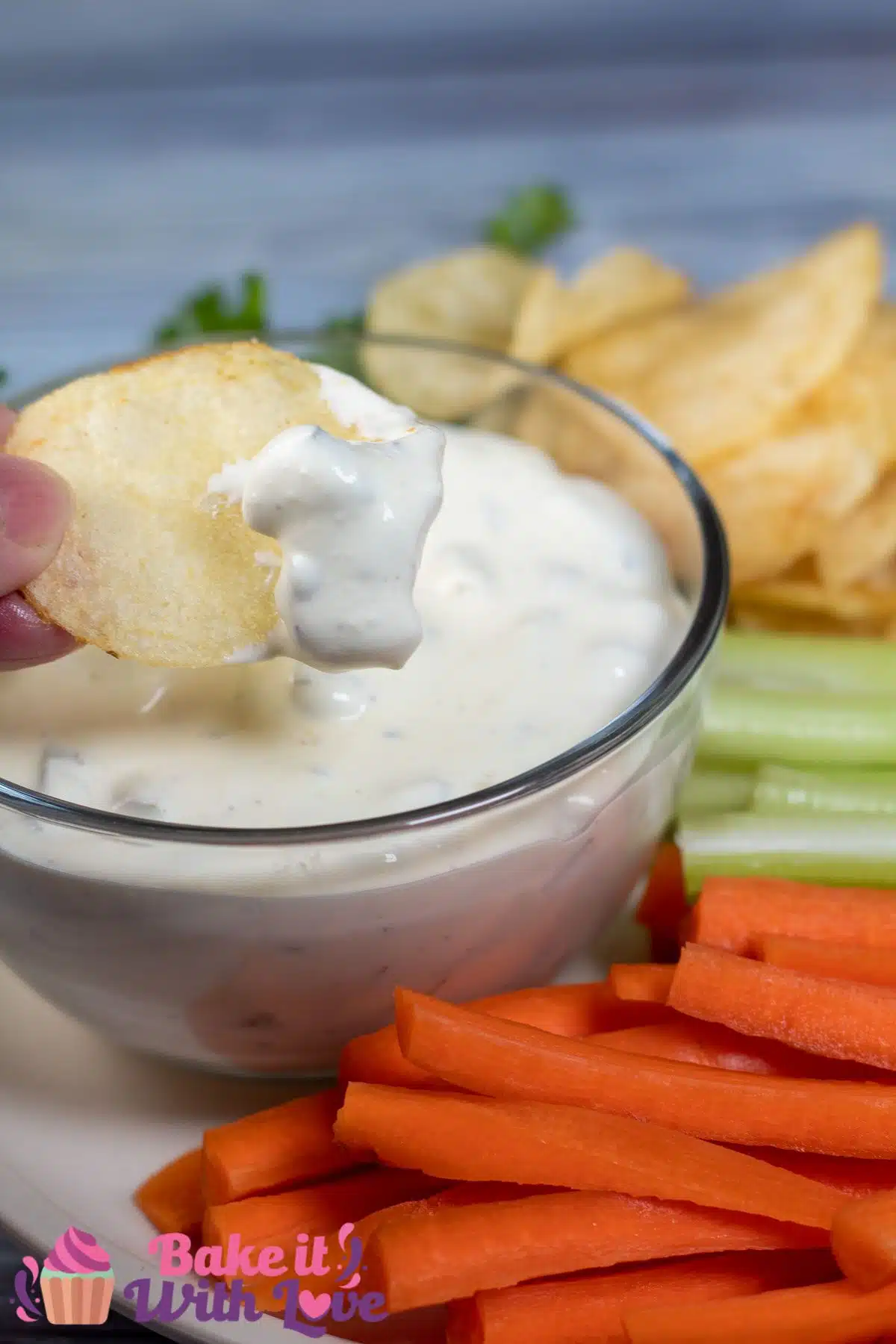 Tall image showing dill pickle dip with carrots, chips, and celery.