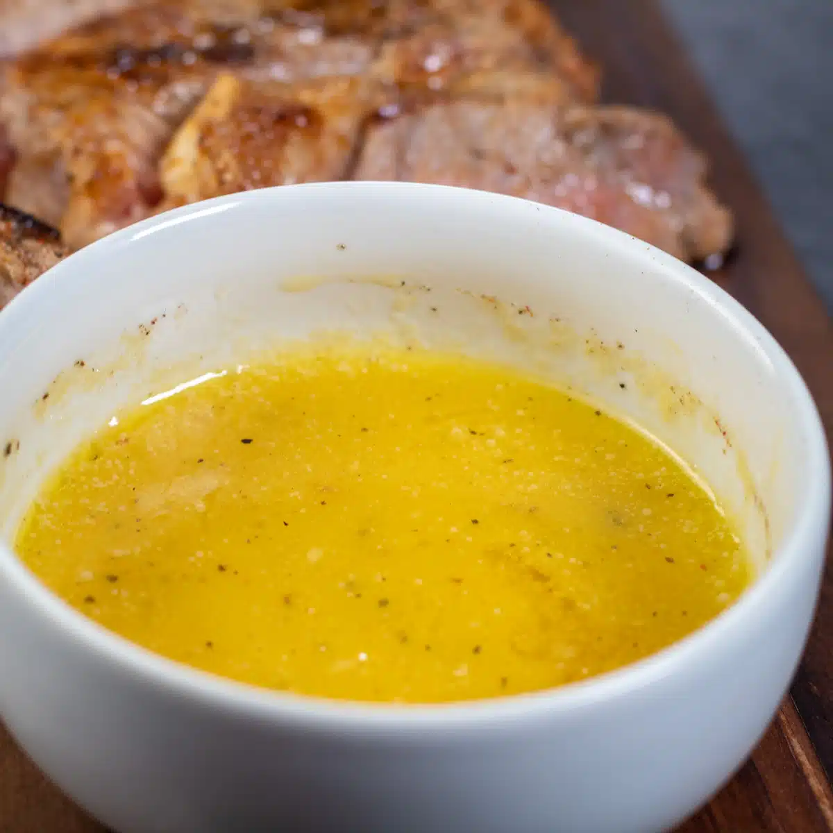 Square image of steak being dipped into garlic butter sauce.