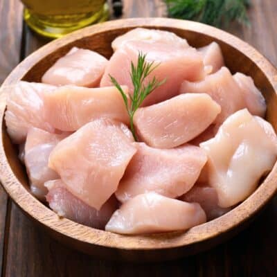 Square image showing raw cut up chunks of chicken breast.