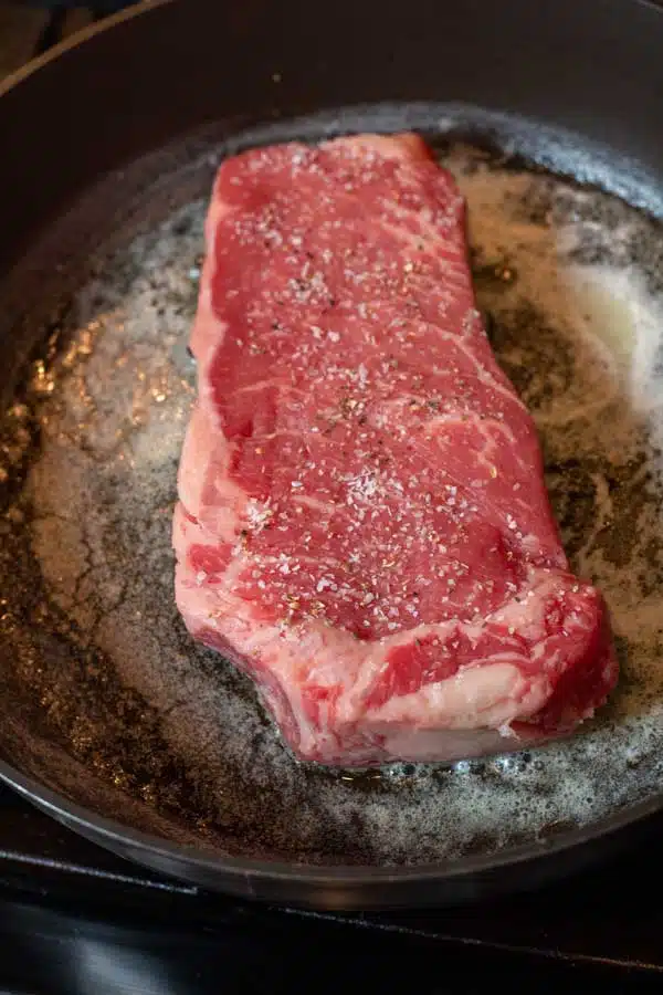 Process image 2 showing seasoned steak cooking in pan.