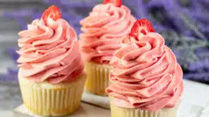 Wide image of cupcakes with strawberry cream cheese frosting on top.