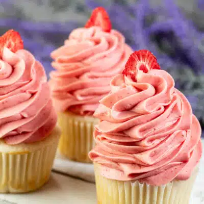 Square image of cupcakes with strawberry cream cheese frosting on top.