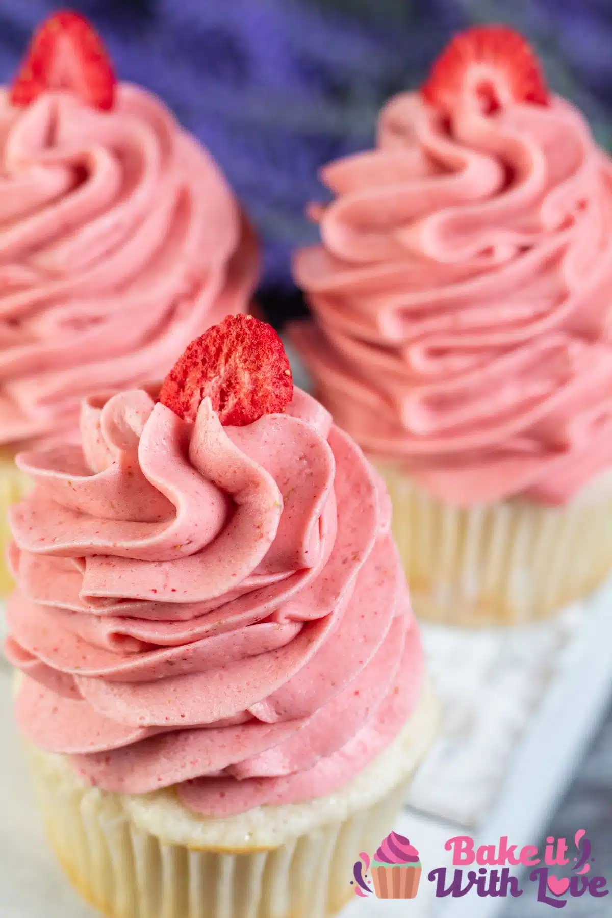 Tall image of cupcakes with strawberry cream cheese frosting on top.
