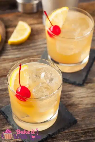 Tall image showing a whiskey sour in a tumbler glass with a cherry.