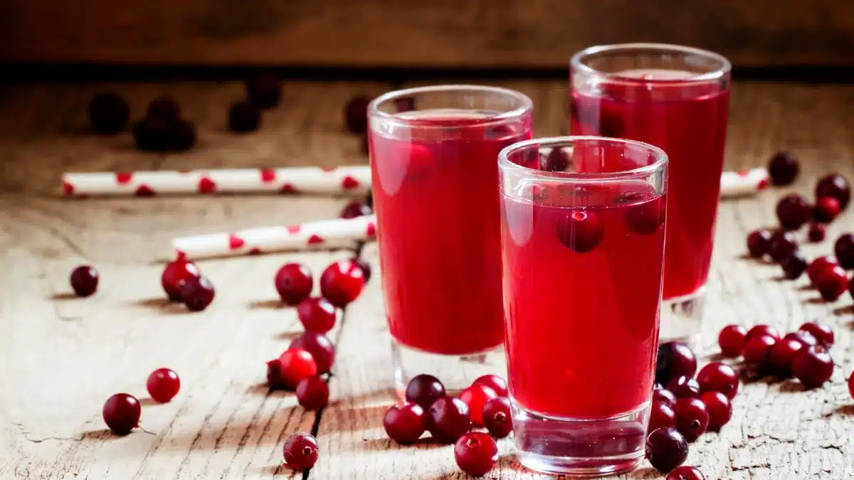 Cranberries are shown here in juice and with fresh berries scattered on wooden background for fruits that start with the letter C.