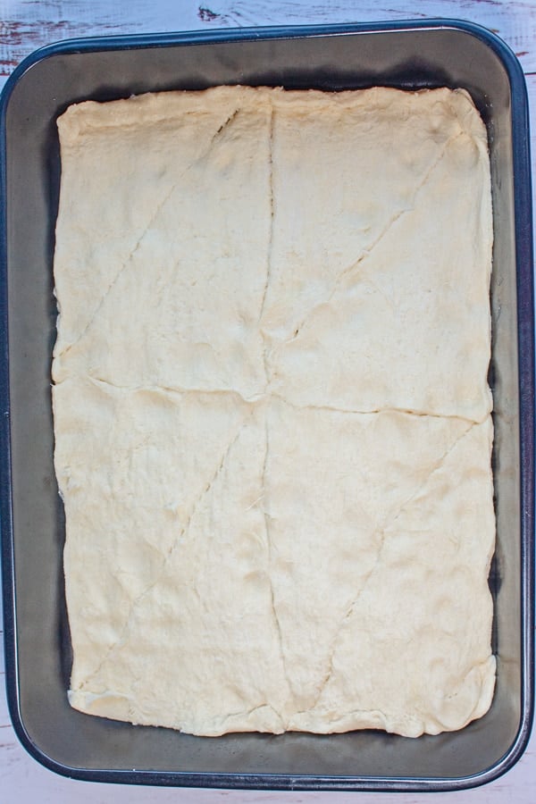 Sopapilla cheesecake bars procesfoto 3 fordel den første nedkølede dåse med halvmåneruller i bunden af ​​en 9x13 bageform.