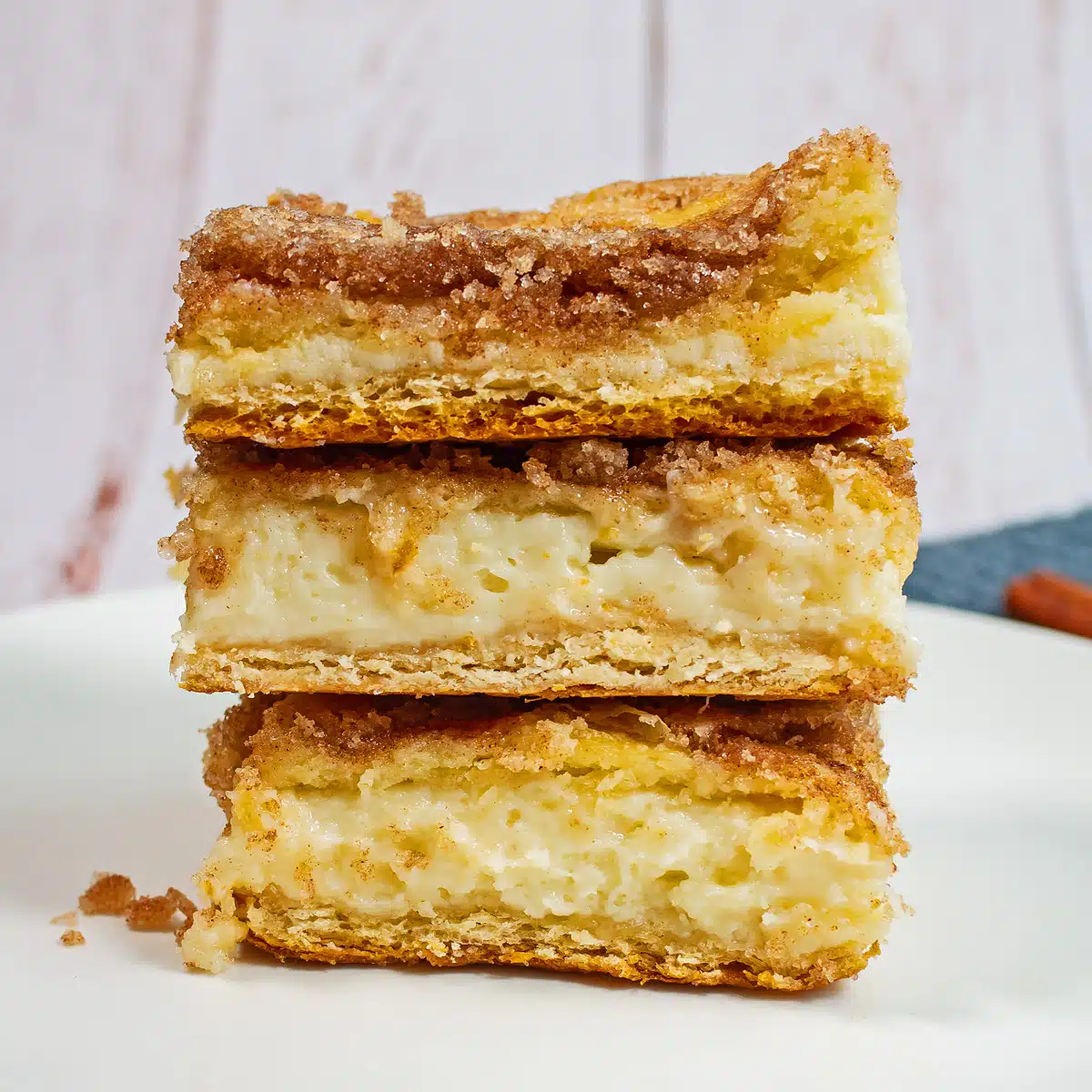 Best sopapilla cheesecake bars recipe with three tasty golden cinnamon coated bars stacked on white plate.