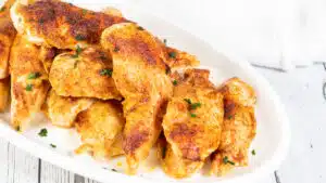 Wide image of baked chicken tenderloins on a white platter.