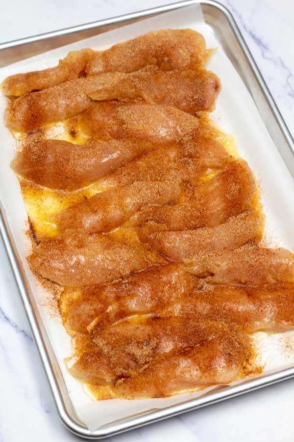 Elaborare l'immagine 5 che mostra i filetti di pollo su una teglia con condimento.
