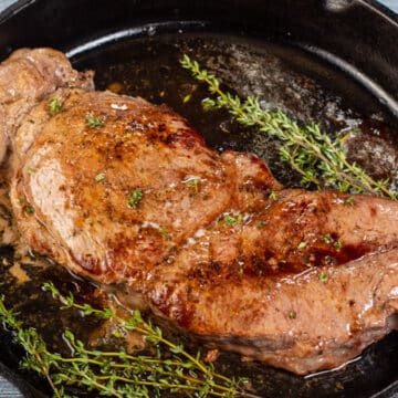 Wide image of baked chuck steak in a cast iron pan.