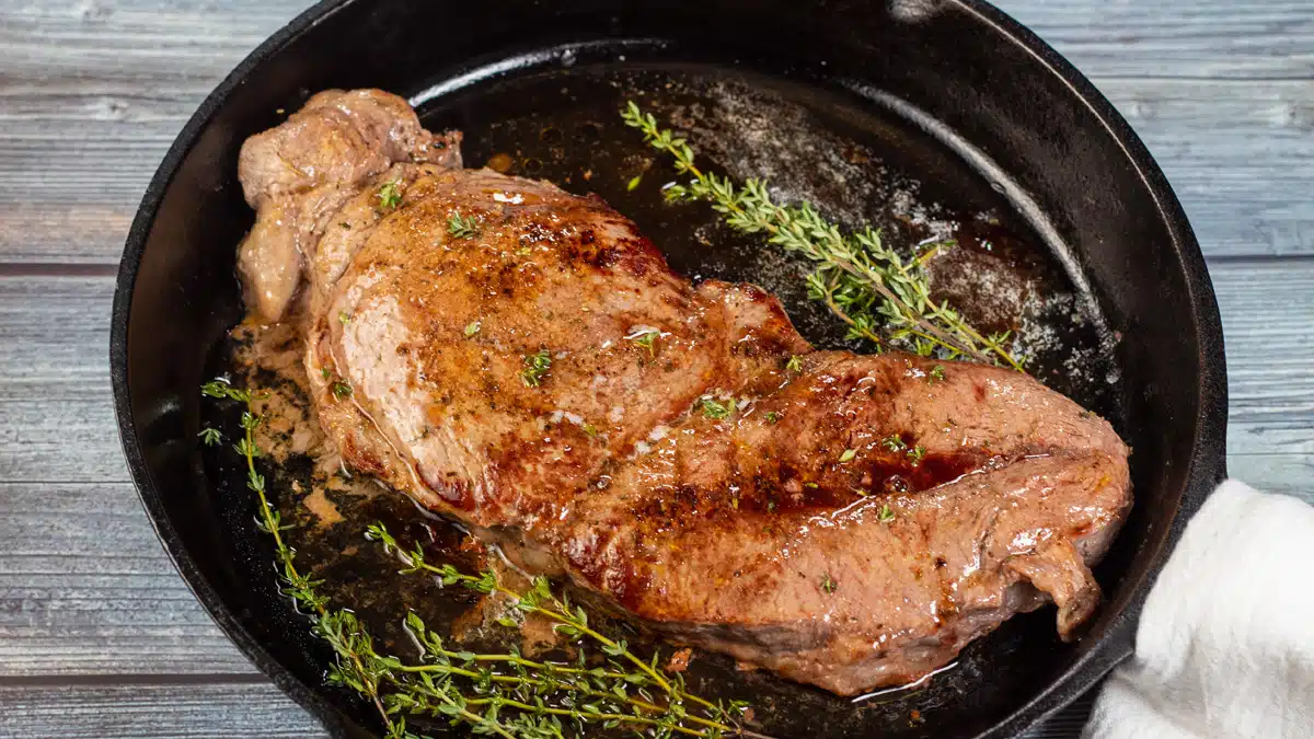 Wide image of baked chuck steak in a cast iron pan.