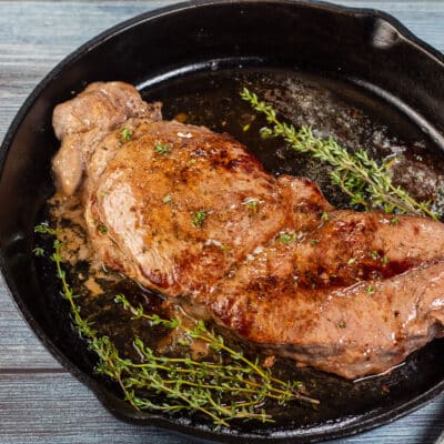 Square image of baked chuck steak in a cast iron pan.