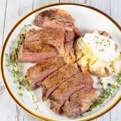 Square image showing sliced baked ribeye steak on a plate with a baked potato.
