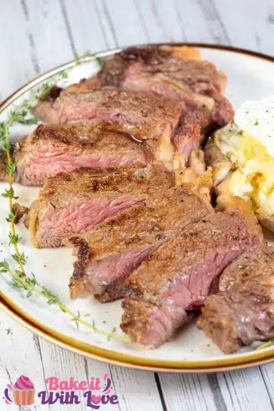 Tall image showing sliced baked ribeye steak on a plate with a baked potato.