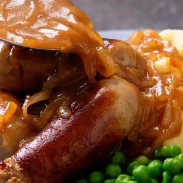 Wide image of bangers and mash, onion gravy, and peas on a plate.