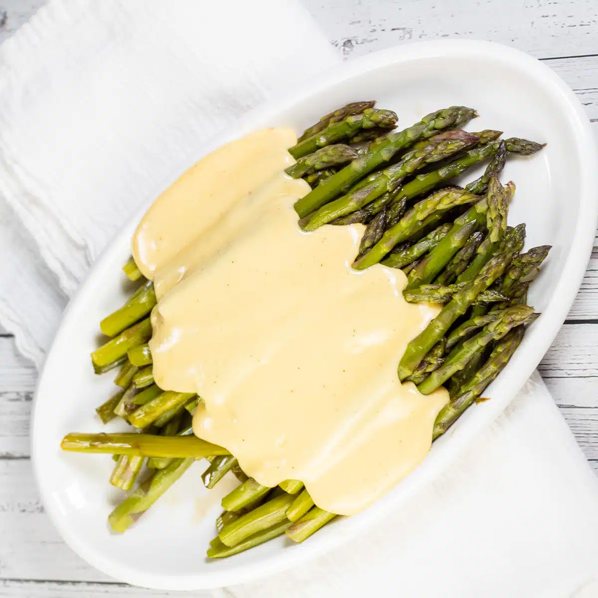 Square image showing cheese sauce on asparagus.