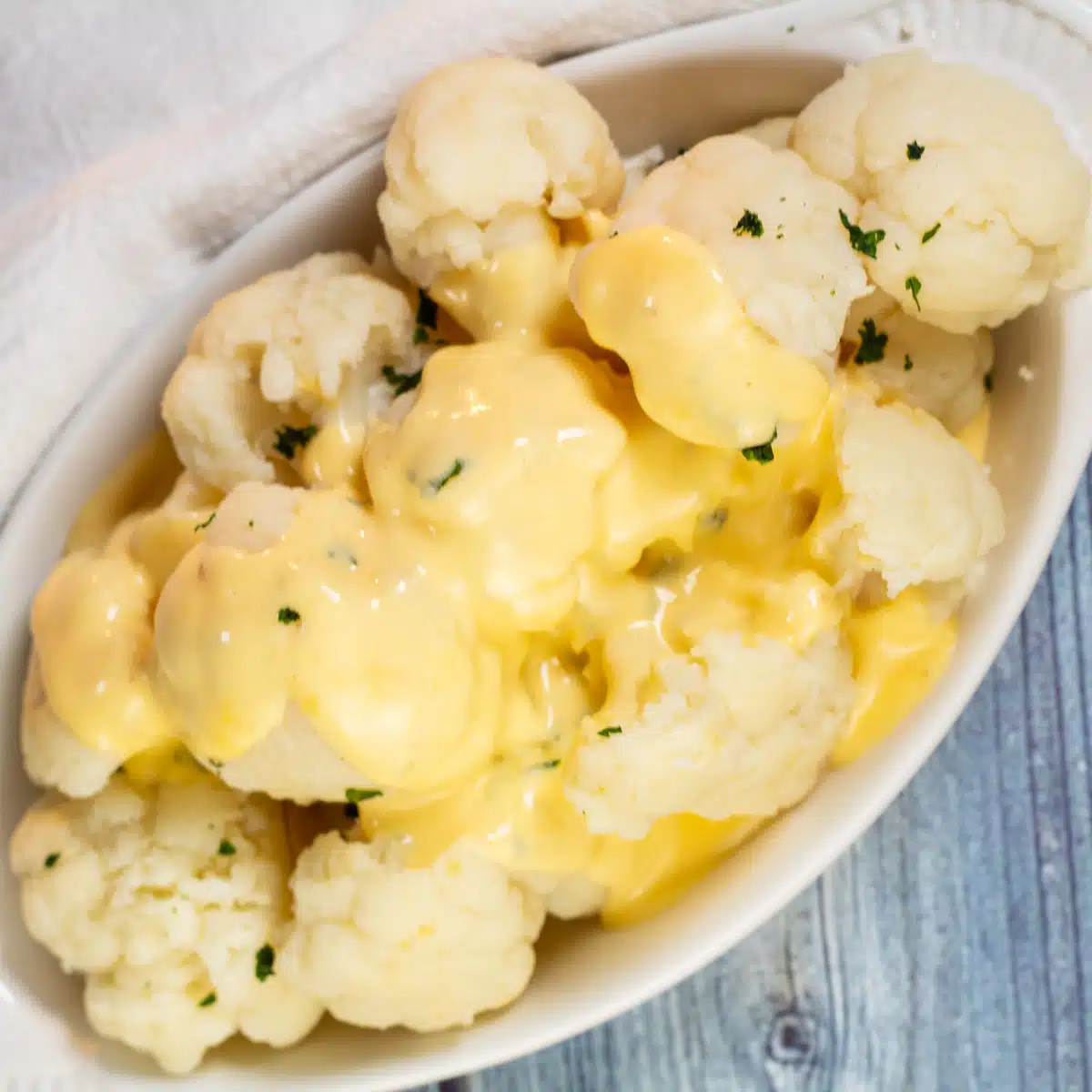 Square image of cauliflower covered with cheese sauce.