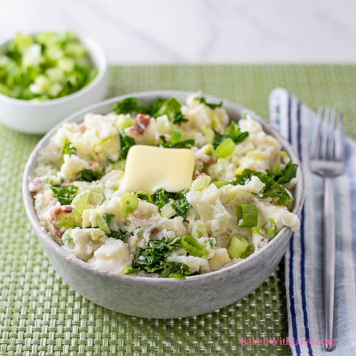 Square image of colcannon in a bowl with chopped green onions in a bowl in the background.