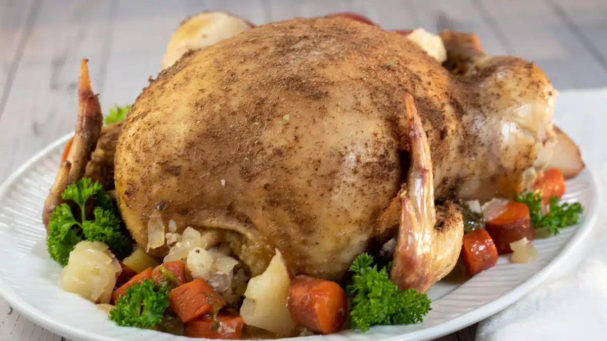 Wide image showing a crockpot cooked whole chicken on a serving platter with mixed veggies.