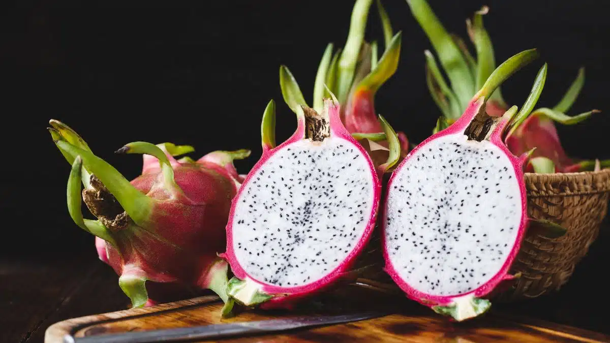 Delicious dragonfruit in a basket with two halves of cut fruit in the front on black background.