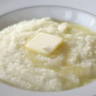 Square image of a bowl of grits with a pat of butter on top.