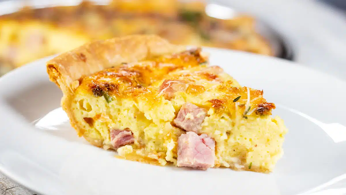 Wide image of a slice of a ham and cheese quiche.