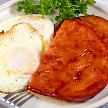 Wide image of ham steaks with eggs on a plate.