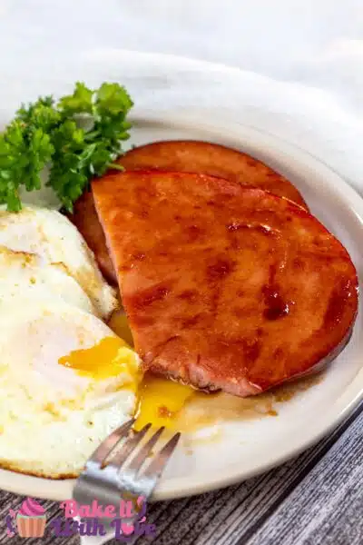 Tall image of ham steaks with eggs on a plate.
