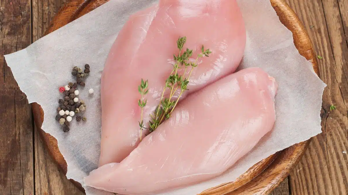 Wide image showing raw chicken breasts.