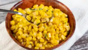 Wide image showing cooked canned corn in a wooden bowl.