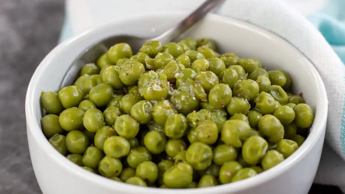Wide image showing canned cooked peas in a small white bowl.