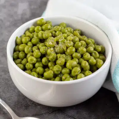 Square image showing canned cooked peas in a small white bowl.