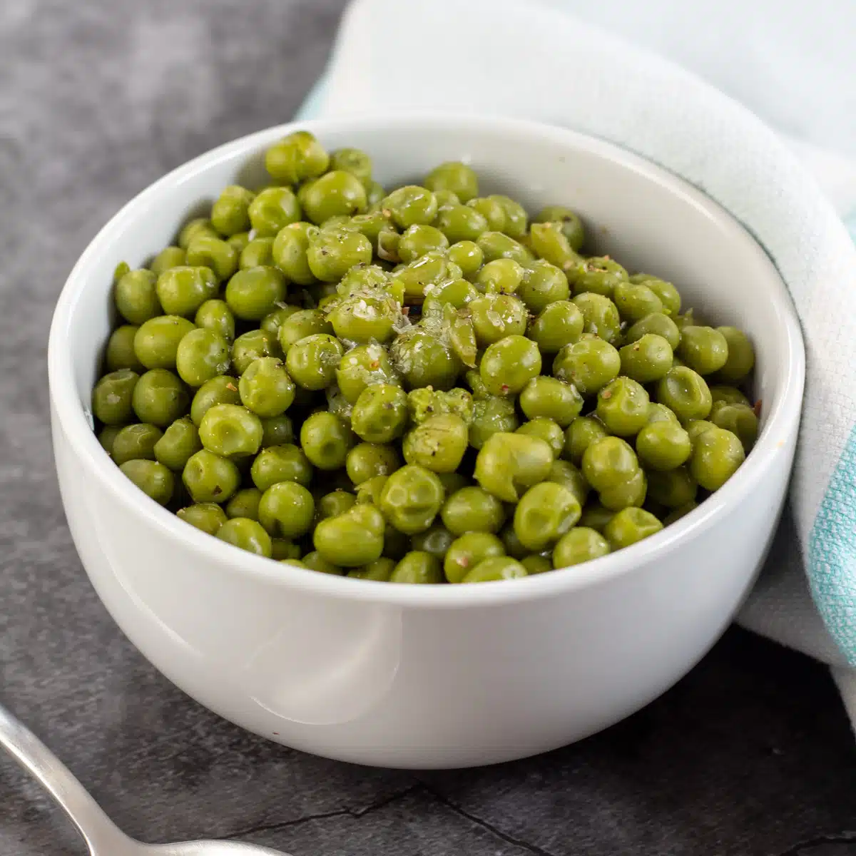 Square image showing canned cooked peas in a small white bowl.