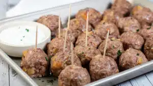 Wide image showing lamb meatballs on a metal tray with dipping sauce.